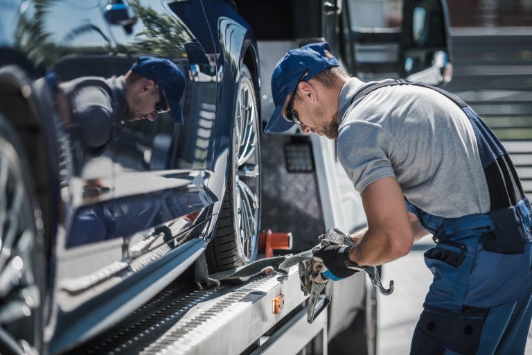 Worker preparing vehicle for safe transport as part of professional towing services.